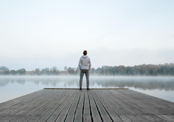 Young,man,standing,alone,on,wooden,footbridge,and,staring,at